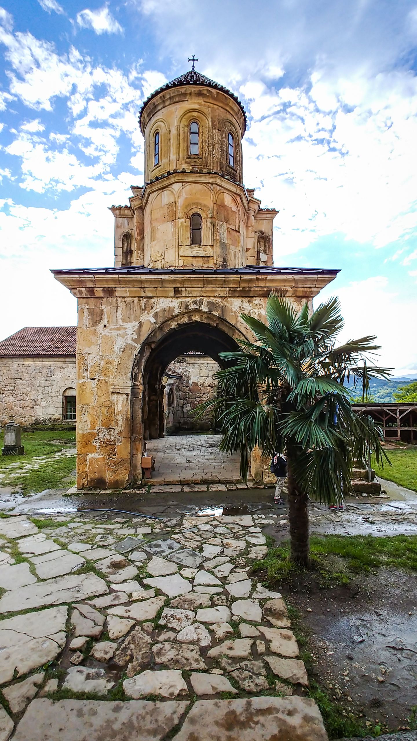 Chiesa di Mtskheta con sentiero in pietra e alberi sotto un cielo limpido in Georgia.